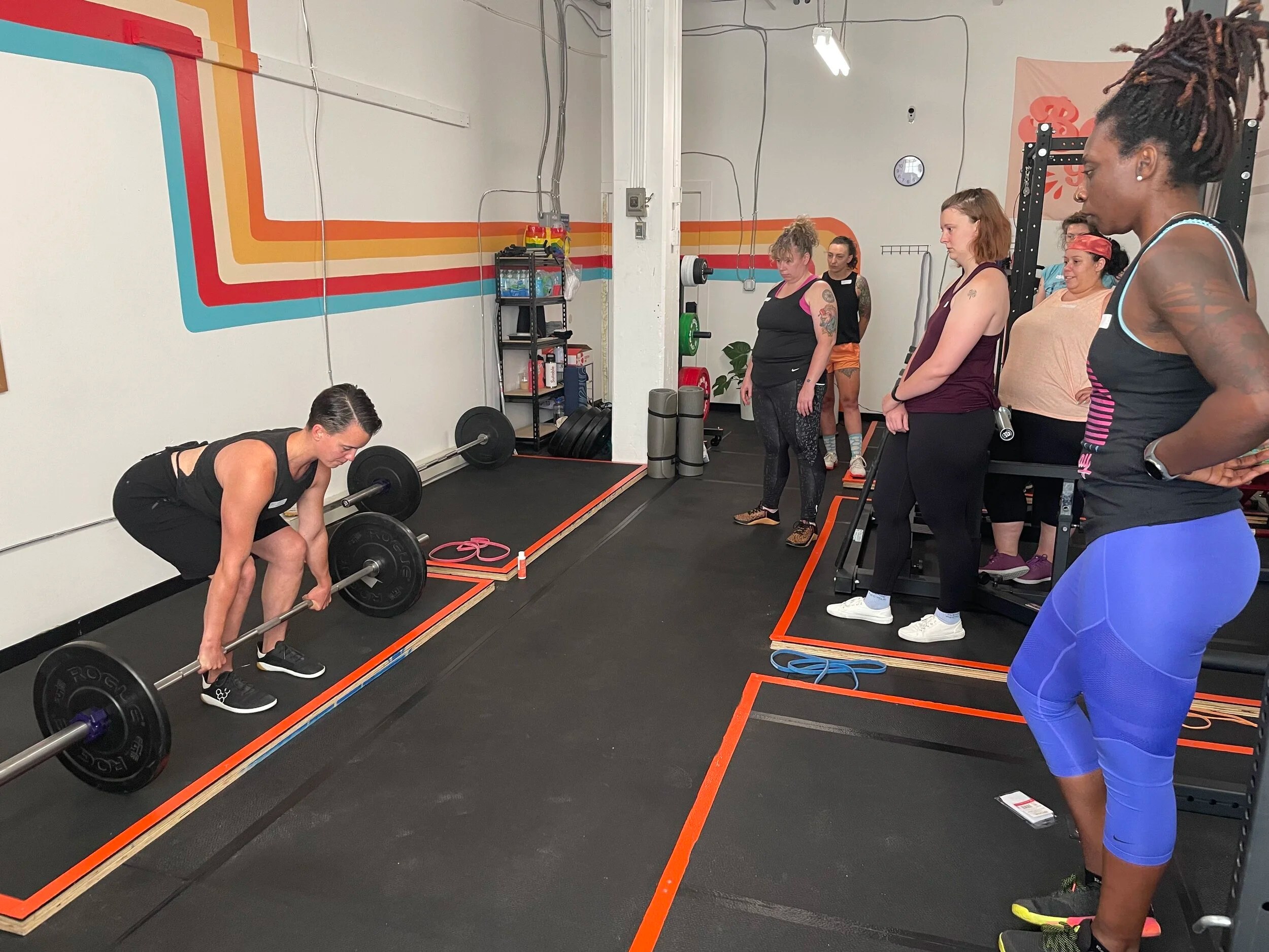 Person lifting a barbell in a gym with onlookers