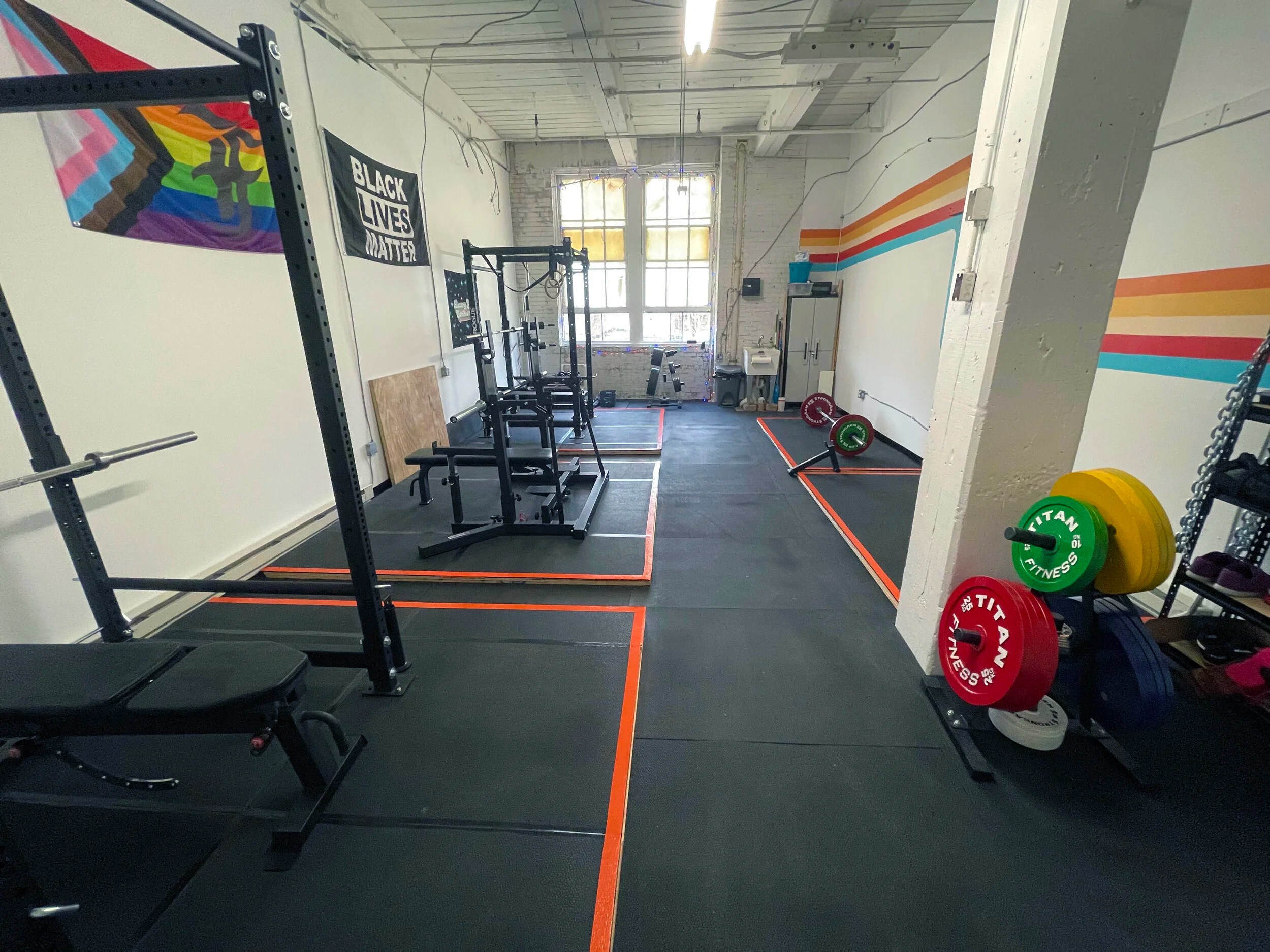 Interior of a gym with weightlifting equipment, colorful weight plates, and motivational banners.