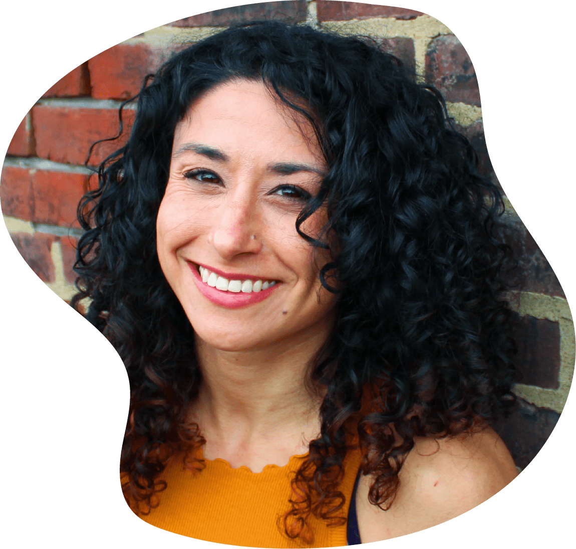  A headshot of Leah, one of the three co-owners of Collective Strength. She is looking into the camera, smiling. A brick wall is in the background.  