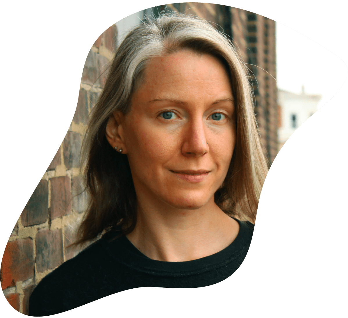  A headshot of Kelly, one of the three co-owners of Collective Strength. Kelly is looking into the camera and smiling. She wears a black long sleeve shirt.  